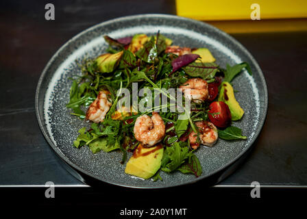 Mann hält einen Teller mit Salat mit Garnelen und Kräuter Stockfoto