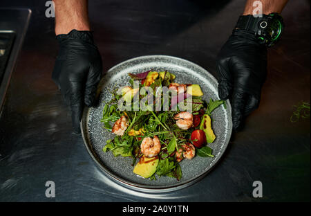 Mann hält einen Teller mit Salat mit Garnelen und Kräuter Stockfoto