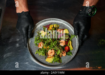 Mann hält einen Teller mit Salat mit Garnelen und Kräuter Stockfoto