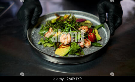 Mann hält einen Teller mit Salat mit Garnelen und Kräuter Stockfoto