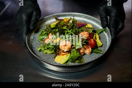 Mann hält einen Teller mit Salat mit Garnelen und Kräuter Stockfoto