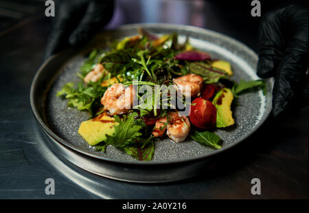 Mann hält einen Teller mit Salat mit Garnelen und Kräuter Stockfoto