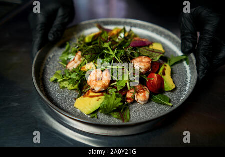 Mann hält einen Teller mit Salat mit Garnelen und Kräuter Stockfoto