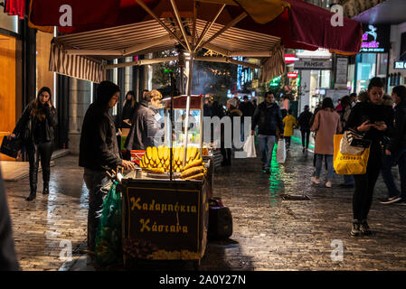 Athen, Griechenland - 31. Dezember 2018: Street Hersteller von glasstrahlperlen, auch als Cob von Mais, mit den Menschen um für Weihnachten in der Nacht in der Mitte der Ader Stockfoto