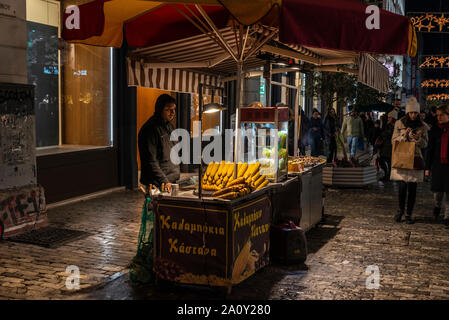 Athen, Griechenland - 31. Dezember 2018: Street Hersteller von glasstrahlperlen, auch als Cob von Mais, mit den Menschen um für Weihnachten in der Nacht in der Mitte der Ader Stockfoto