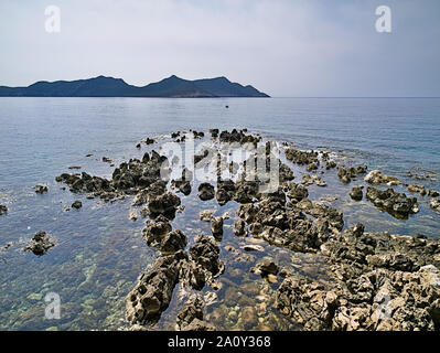 Blick von Küste zu Meer mit scharfkantigen Felsen und Insel im Hintergrund bei bewölktem Himmel, Methoni, Peloponnes, Griechenland. Stockfoto