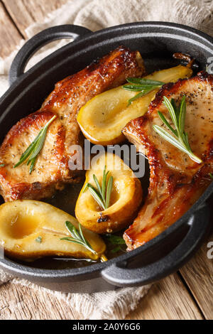 Leckere heiße Schweinskotelett gebacken mit Birnen und Rosmarin in Honig Sauce in einer Pfanne close-up auf dem Tisch. Vertikale Stockfoto