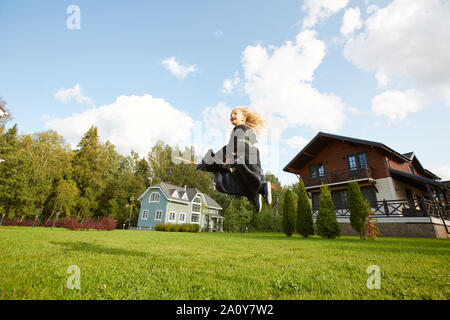 Weitwinkel Portrait von glücklichen kleinen Hexe auf Besen fliegen über dem grünen Rasen in Halloween, kopieren Raum Stockfoto