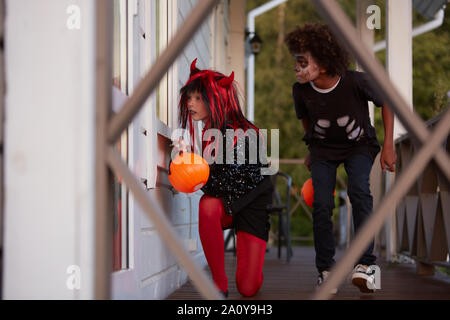 Porträt von zwei sneaky Kinder verstecken ausserhalb des Hauses beim Spielen auf Halloween, kopieren Raum Stockfoto