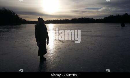 Meine silhouette beim Spaziergang auf dem zugefrorenen See bei Sonnenuntergang in den Vororten von Stockholm Stockfoto