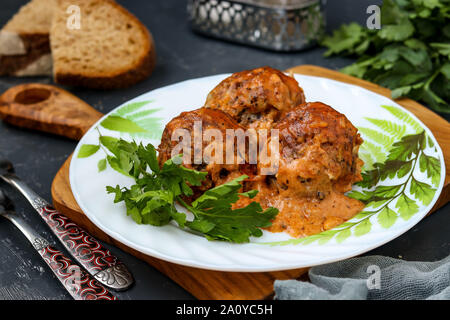 Fleischbällchen in saurer Sahne und Tomaten Sauce in Weiß Platte gegen eine Holzplatte, horizontale Ausrichtung Stockfoto