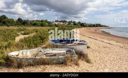 WEST MERSEA, ESSEX, Großbritannien - 31. AUGUST 2018: Der Strand entlang des Flusses Blackwater mit alten Schlauchbooten und Menschen im Hintergrund Stockfoto