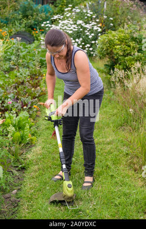 Frau mit schnurlosen (Lithium-Ionen-Akku) strimmer Gras auf dem Weg in die Zuteilung zu schneiden Stockfoto