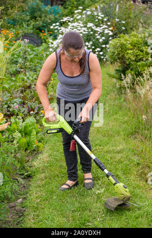 Frau mit schnurlosen (Lithium-Ionen-Akku) strimmer Gras auf dem Weg in die Zuteilung zu schneiden Stockfoto