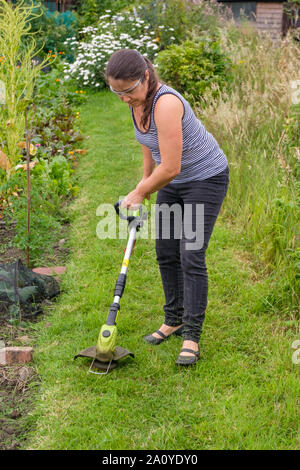 Frau mit schnurlosen (Lithium-Ionen-Akku) strimmer Gras auf dem Weg in die Zuteilung zu schneiden Stockfoto