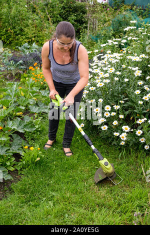 Frau mit schnurlosen (Lithium-Ionen-Akku) strimmer Gras auf dem Weg in die Zuteilung zu schneiden Stockfoto