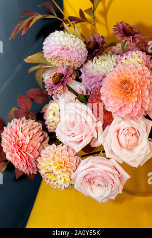Florale Komposition von Dahlia Blumen, Rosen und Blätter im Herbst. Arty, leuchtend rot und rosa Blumenstrauß auf gelbem Hintergrund Stockfoto