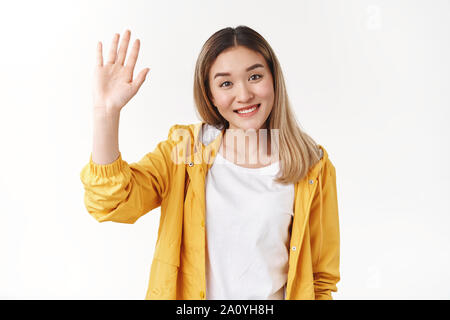 Freundlich nett Fröhlich abgehende asiatische blonde Mädchen heben die Hand hoch fünf Sagen hallo hallo Gruß freudig lächelnd weitgehend toothy positive Grinsen wel Stockfoto