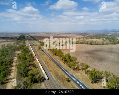 Antenne von gemischten Güterzug durch einen Boom gesteuert Bahnübergang Position entlang der Seite des Bruce Highway Queensland Australien vorbei Stockfoto