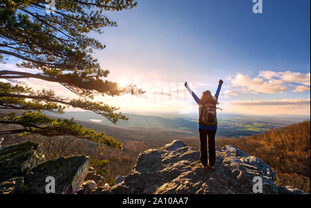 Weibliche Wanderer Anheben der Arme in der Feier zu, wie die Sonne über eine herrliche Aussicht an der Spitze einer Appalachian Mountain im Herbst Stockfoto