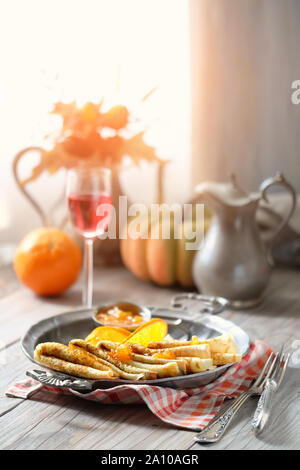 Crepes Suzette auf vintage Metallplatte mit orange Sauce serviert. Köstliches Frühstück mit Herbst Dekorationen auf Holztisch. Stockfoto