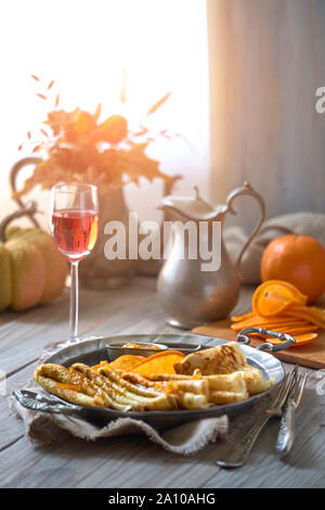 Crepes Suzette auf vintage Metallplatte auf Holztisch mit orange Sauce serviert. Köstliches Frühstück mit Herbst Dekorationen Stockfoto