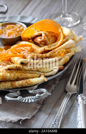 Crepes Suzette auf vintage Metallplatte auf Holztisch mit orange Sauce serviert, close-up auf einer Platte Stockfoto