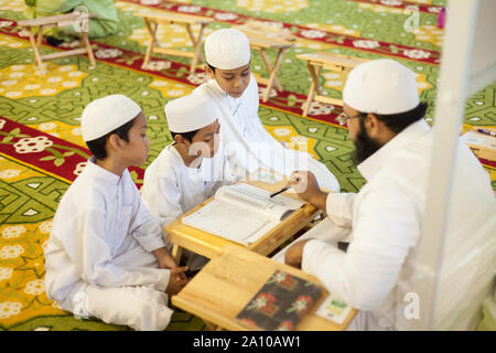 Ein erwachsener Religion Lehrer unterrichten von Kindern studieren im Inneren Masjid Moschee, Singapur Stockfoto