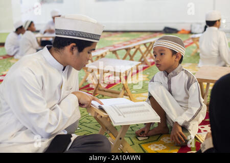 Ein jüngeres Malay teenager Lehre ein sehr junges Kind Studieren im Inneren Masjid Moschee, Singapur Stockfoto