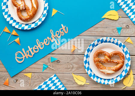 Oktoberfest, flach auf rustikalen Holztisch mit blauen Papier verteilt, Brezeln auf das verfügbare Platten, Weizenähren, dekorationsfahnen und Blätter im Herbst Stockfoto