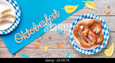 Oktoberfest, flach auf rustikalen Holztisch mit blauen Papier verteilt, Brezeln auf das verfügbare Platten, Weizenähren, dekorationsfahnen und Herbstlaub, Pa Stockfoto