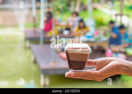 Hand Kuchen unscharfen Hintergrund Menschen und Baum im Garten am Teich. Stockfoto