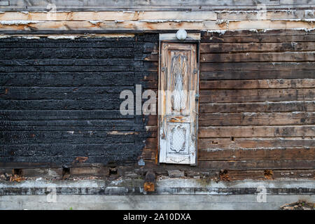 Die Wand eines Holz- Haus aus Holz ist die Hälfte verbrannt nach einem Brand und mit schwarzer Kohle in der Mitte ist eine schmale Tür. Cataclys Stockfoto