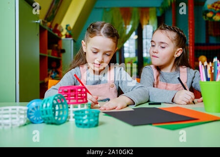 Zwei kleine Zwillingsschwestern zeichnen und fröhlich verbringen viel Zeit in das Spiel Zimmer Stockfoto