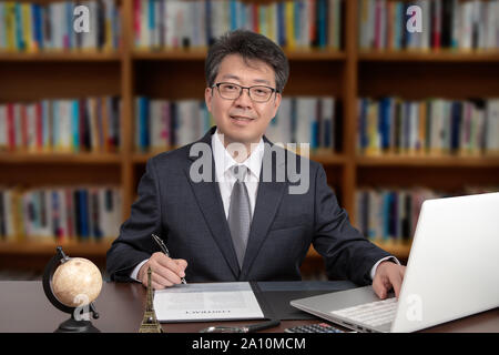 Ein Porträt eines asiatischen im mittleren Alter Mann Geschäftsmann an einem Schreibtisch sitzen Stockfoto