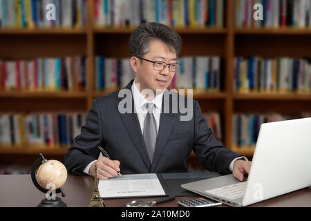 Ein Porträt eines asiatischen im mittleren Alter Mann Geschäftsmann an einem Schreibtisch sitzen Stockfoto