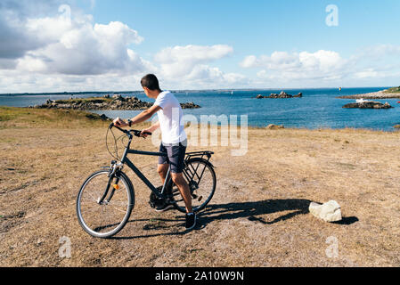 Attraktive junge männliche Fahrten mit dem Fahrrad genießen Sie die Aussicht auf die Landschaft auf der Insel Batz Stockfoto