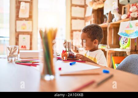 Schöne afrikanische amerikanische Kleinkind spielen mit Dinosaurier Spielzeug auf dem Schreibtisch im Kindergarten Stockfoto