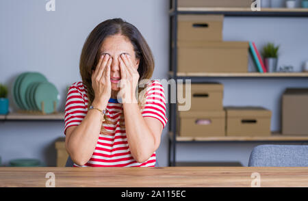 Mittleren Alters ältere Frau am Tisch zu Hause sitzen die Augen reiben für Ermüdung und Kopfschmerzen, schläfrig und müde Ausdruck. Vision Problem Stockfoto