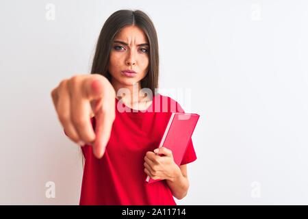 Junge hübsche Studentin Frau mit roten Buch über isoliert weißer Hintergrund mit dem Finger an die Kamera und an Sie gerichtet, Handzeichen, posit Stockfoto
