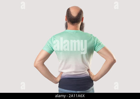 Rückseite Porträt der glatzköpfige Mann mittleren Alters mit Bart in hellem Grün t-shirt auf den Taillen. indoor Studio shot, isoliert auf Grau backgr Stockfoto