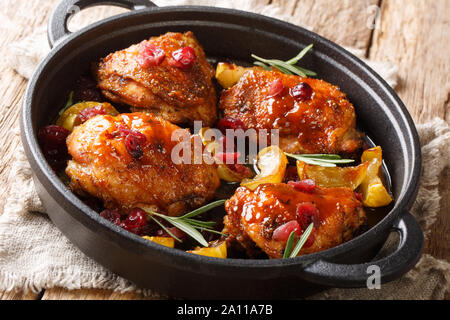 Landhausstil gebackene Hühnerkeule mit Äpfeln, Preiselbeeren und Rosmarin close-up in einer Pfanne auf dem Tisch. Horizontale Stockfoto