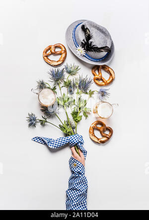 Oktoberfest layout Komposition mit Becher Bier, bayerische hut mit feder, Brezel, Frau Hand in traditionellen Blau Bluse und Alpenblumen. Top vi. Stockfoto