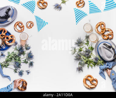 Oktoberfest Hintergrund. Becher Bier, bayerische Hüte mit Feder, Brezel, Frau Hände in traditionellen Blau Bluse und alpin Blumen. Ansicht von oben. Modern. Stockfoto