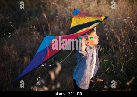 Glücklich gesund süssen Träumen kleine Kind mit Spielzeug bunte Drachen hinter den Schultern stehend unter trockenes Gras auf warmen Sonnenuntergang über Flug denken Stockfoto