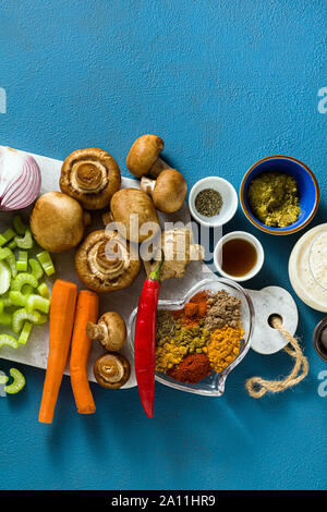 Zutaten für das Kochen Indischer aus Gemüse, Kürbis und Pilze auf einem blauen Hintergrund und Gewürze Curry. Schuss von oben. Kopieren Sie Platz Stockfoto