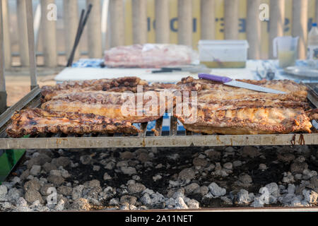 BBQ-Rack von Rippchen aufgereiht auf einem großen Grill mit Rauch aus dem Feuer unter. Stockfoto