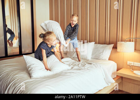 Adroable kleiner Bruder und Schwester lachend, während eine Kissenschlacht zusammen auf ihrem Bett zu Hause Stockfoto