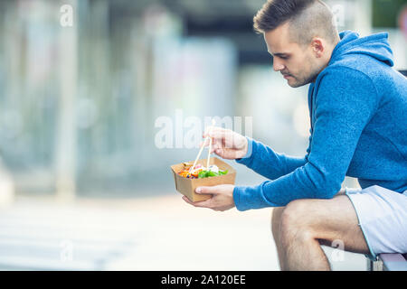 Junger Mann zu Mittag essen, asiatische Küche, von Recyclingpapier. Stockfoto