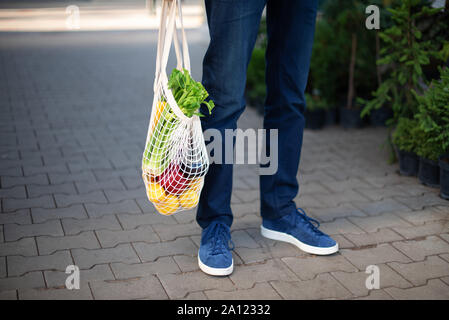 Mann hält mesh Einkaufstasche mit Gemüse ohne Plastiktüten bei Farmers Market. Null Abfall, Kunststoff Konzept. Nachhaltiger Lebensstil. Stockfoto